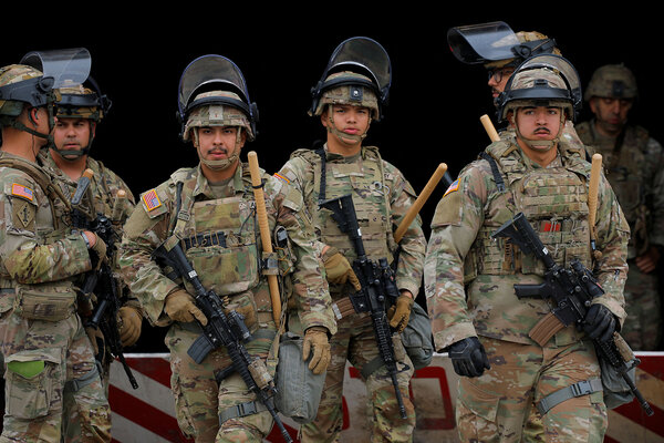 Members of the California National Guard wearing camoflage uniforms, riot helmets and rifles, stand together.