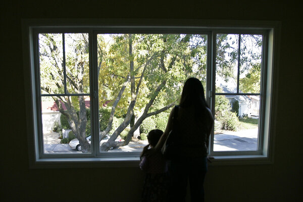 A mother and child look out a large window at a view of a tree outside. 